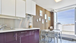 A modern kitchen with white cabinets, a purple countertop, and a dining area with a table and chairs. - Appartement avec terrasse ensoleillée sur le port Olona (Les Sables-d'Olonne)