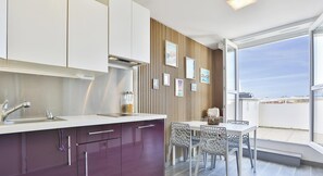 A modern kitchen with a dining area, large windows, and a view of the city. - Appartement avec terrasse ensoleillée sur le port Olona (Les Sables-d'Olonne)