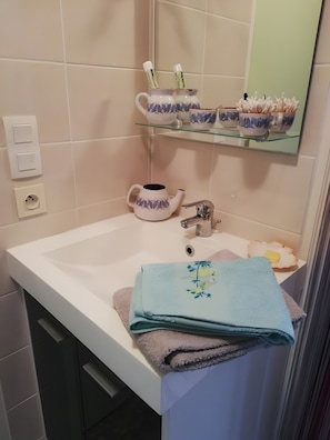 Une salle de bain avec un lavabo blanc, un miroir, un porte-serviettes avec des serviettes pliées et une étagère contenant des articles de toilette.