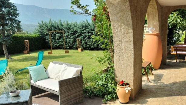 A patio area with a wicker sofa, a glass table, a potted plant, and a large terracotta pot. - Guest Room “La Grande Calade” with Mountain View, Terrace and Wi-Fi (Garde-Colombe)