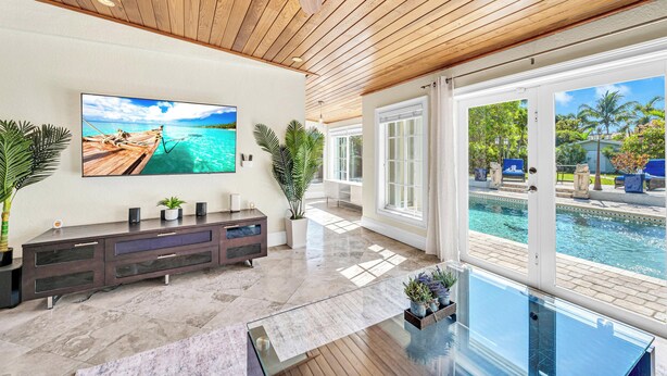 A spacious living room with a large TV, wooden ceiling, and a view of a swimming pool. - Spacious Tropical Pool Home Miami. 4/3. Sleeps 13. Large Garden/ Backyard. (Miami)