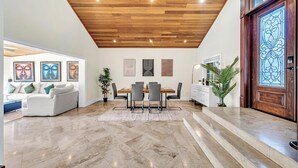 A modern interior with a wooden ceiling, a dining area with a table and chairs, and a large decorative door. - Spacious Tropical Pool Home Miami. 4/3. Sleeps 13. Large Garden/ Backyard. (Miami)