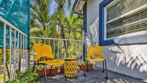 Un balcon avec des chaises jaunes, une table ronde et des plantes en pot.
