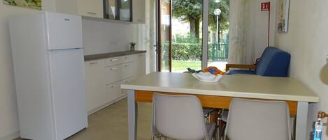 A compact kitchen with a refrigerator, a dining table with two chairs, and a view of the outdoors through a glass door.