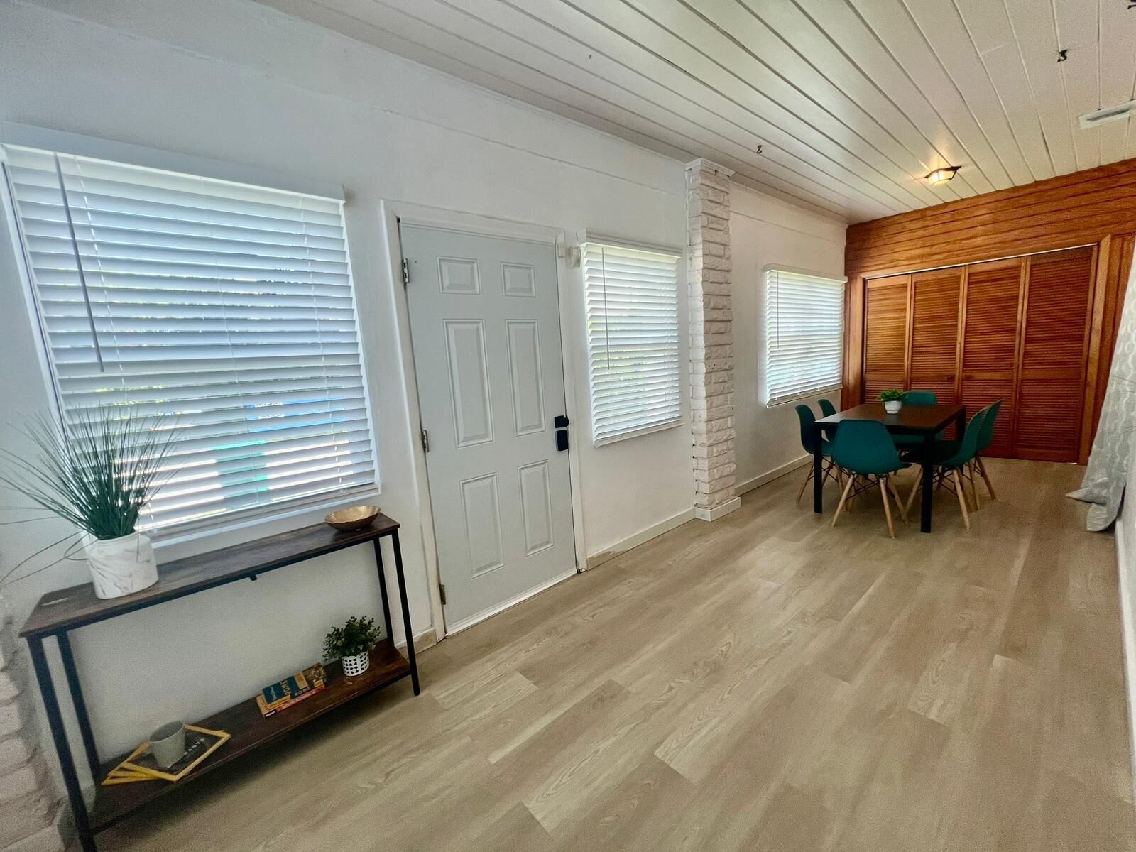 Une pièce avec un plancher en bois, une table à manger avec des chaises, une porte blanche et un mur recouvert de lambris en bois.