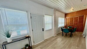 Ett rum med trägolv, ett matbord med stolar, en vit dörr och en vägg med träpanel.