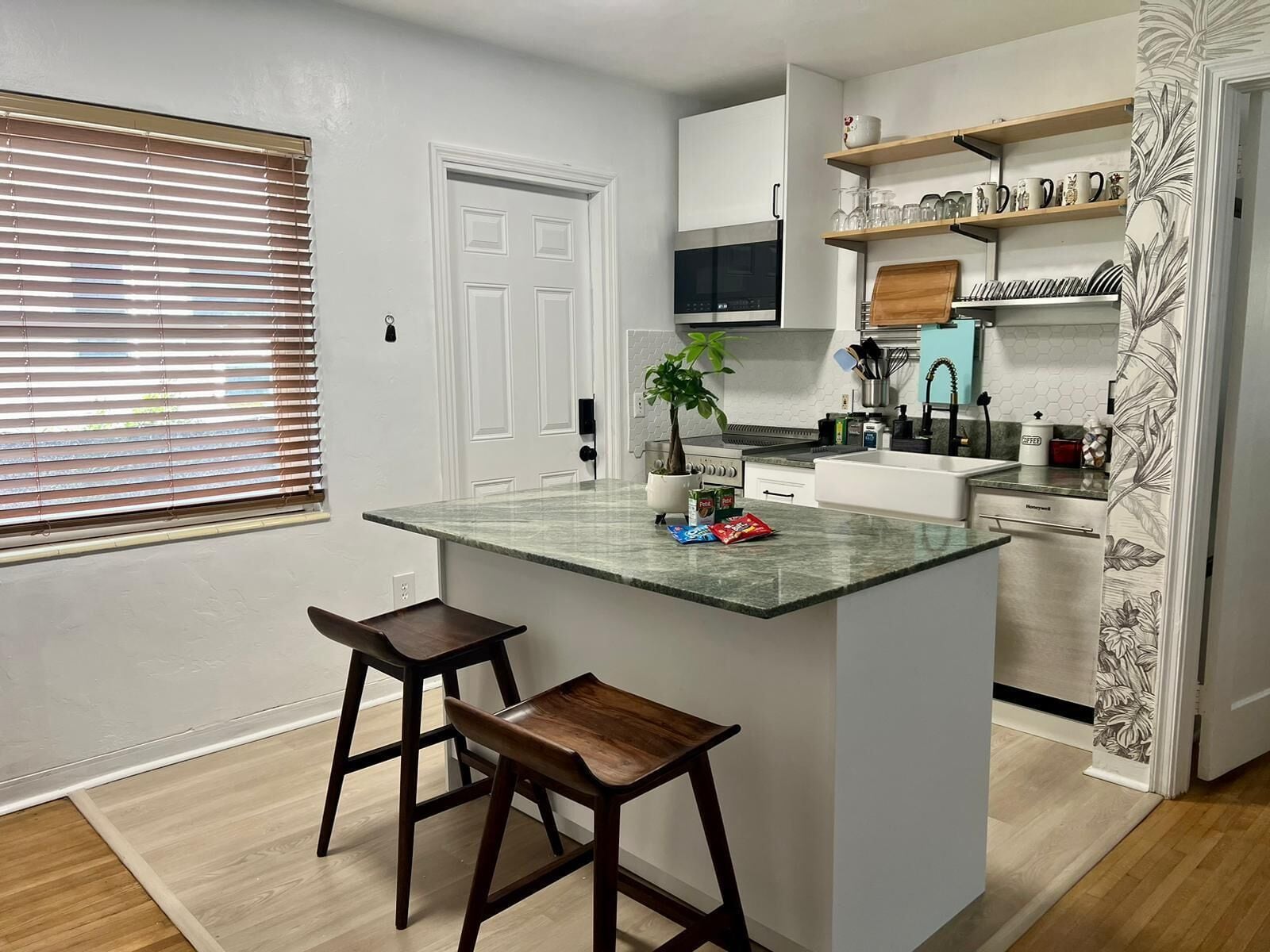 A modern kitchen with a central island, wooden stools, a built-in oven, and a microwave.