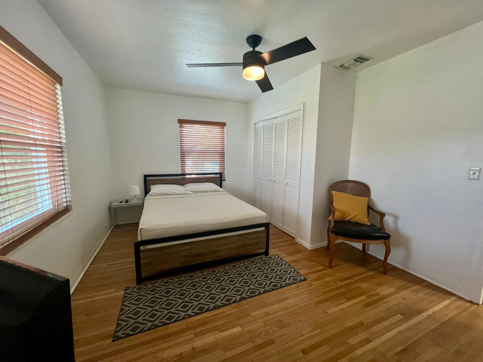 A bedroom with a bed, a nightstand, a chair, a ceiling fan, and a wardrobe.