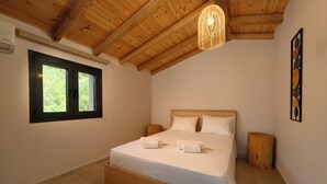 Une chambre avec un plafond en bois, un lit recouvert de draps blancs, deux tables de chevet, une fenêtre et une œuvre d’art accrochée au mur.