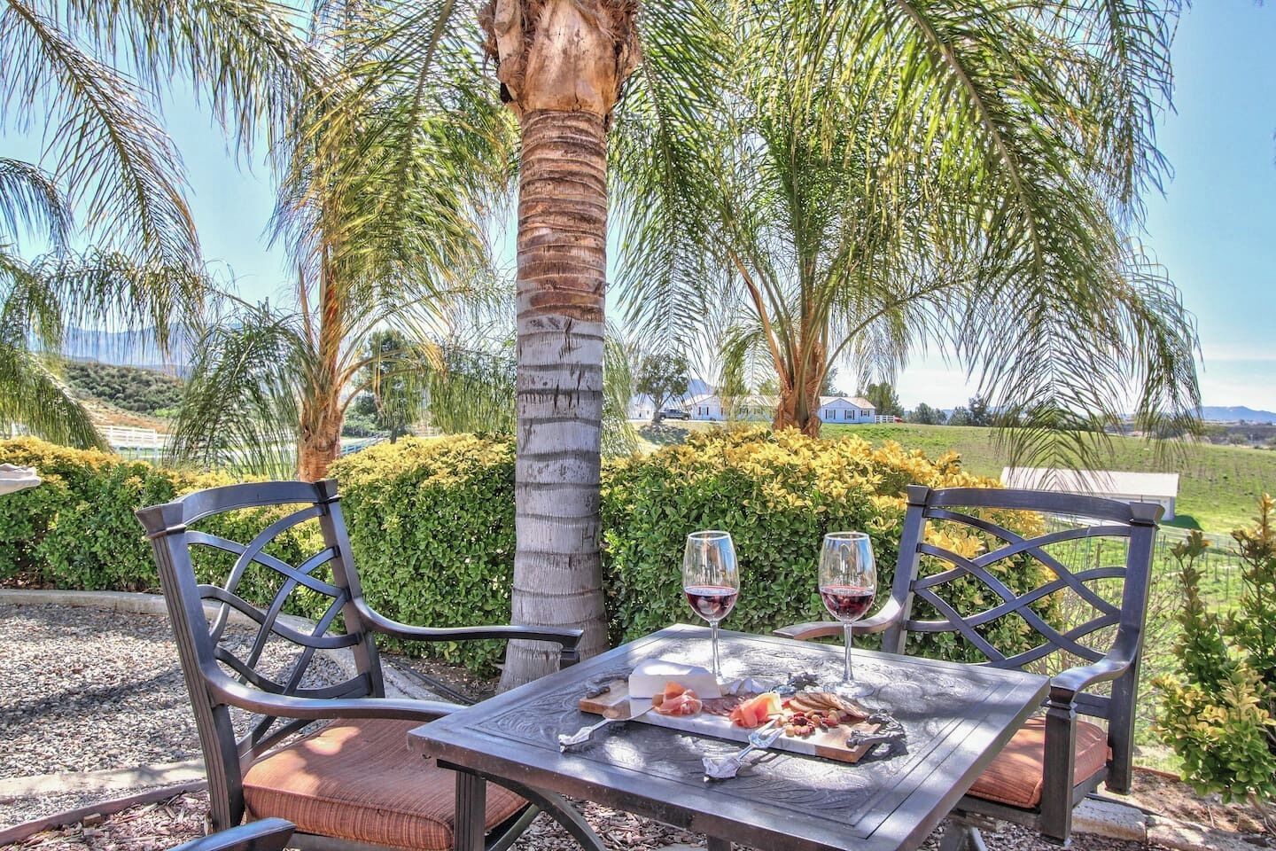 An outdoor dining area with a table set for two, surrounded by palm trees and greenery.