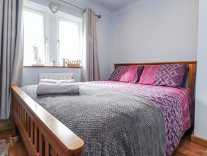 A bedroom with a wooden bed frame, a grey and pink patterned bedspread, a white radiator, and a window with curtains. - 2 Rock View (Settle)