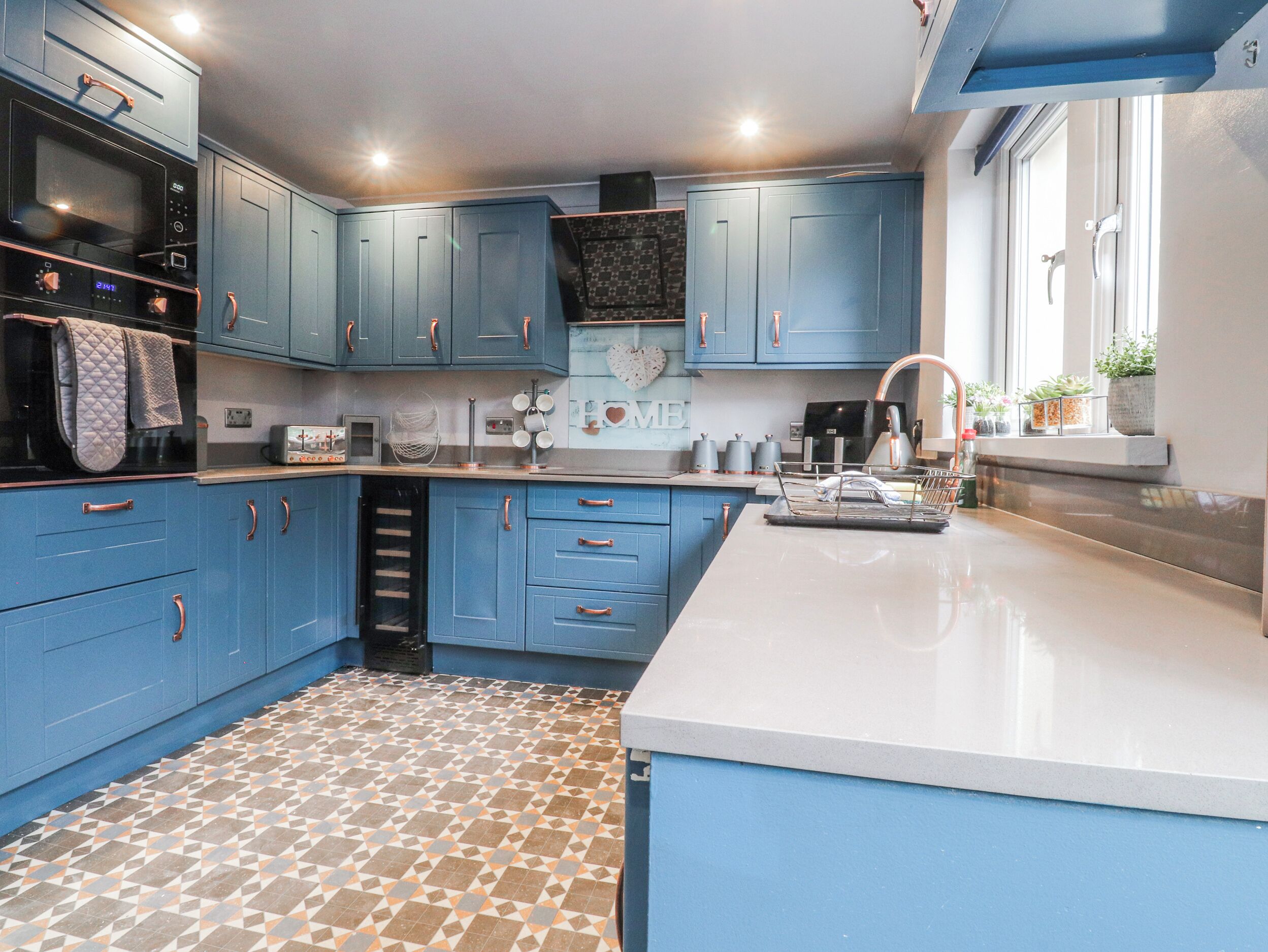 A kitchen with blue cabinets, a microwave, a coffee maker, and a clock on the wall.