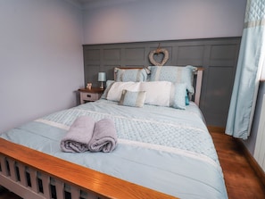 A neatly made bed with a headboard, a nightstand with a lamp, and a heart-shaped decoration on the wall. - 2 Rock View (Settle)