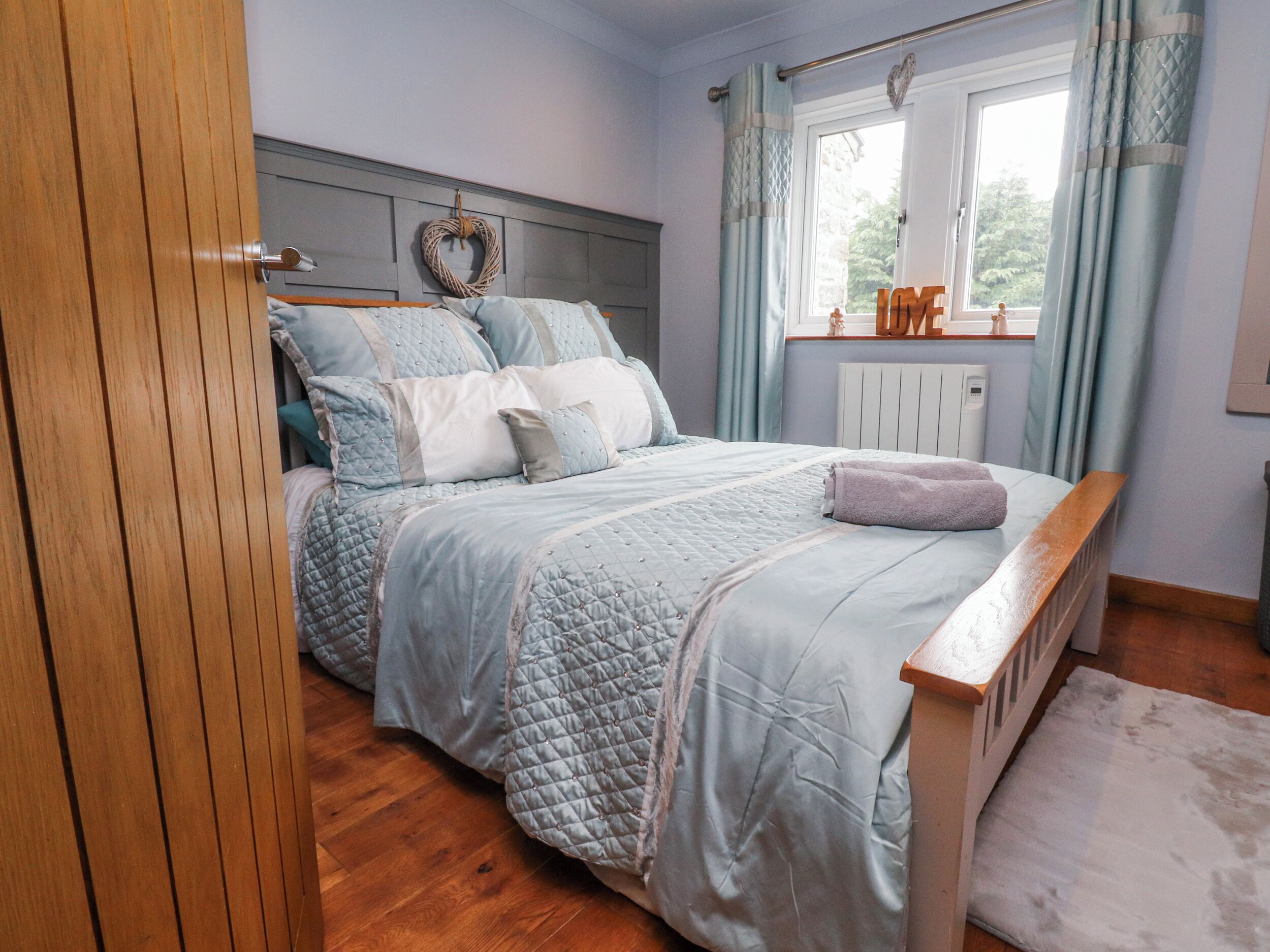 A bedroom with a wooden bed frame, a quilted bedspread, a white radiator, and a window with curtains.