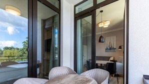 A balcony with a table and chairs, a sliding glass door leading to a dining area, and a view of greenery. - 4 Star Holiday Home in Travemunde (Lübeck)