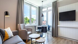 A modern living room with a sofa, armchair, round tables, a TV, and large windows. - 4 Star Holiday Home in Travemunde (Lübeck)