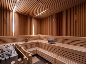 A sauna room with wooden slatted walls, benches, and a stone basin. - 4 Star Holiday Home in Travemunde (Lübeck)