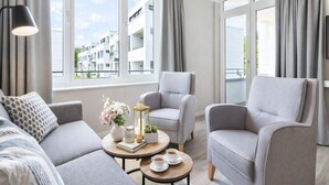 A modern living room with a sofa, armchairs, a coffee table, and a view of residential buildings. - 4 Star Holiday Home in Travemunde (Lübeck)
