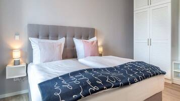 A bedroom with a bed, bedside lamps, a wardrobe, and a bedside table.