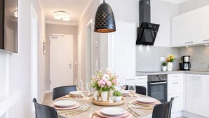 A modern kitchen with white cabinets, a black range hood, and a dining area with a round table set for four. - 4 Star Holiday Home in Travemunde (Lübeck)