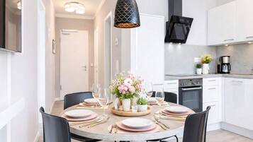 A modern kitchen with white cabinets, a black range hood, and a dining area with a round table set for four.