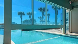 A swimming pool with clear blue water, large windows, and palm trees in the background. - Tradewinds #1108 - Beachfront 1BR + Bunks, Gulf View, Indoor/Outdoor Pool (Orange Beach)
