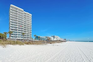 A beachfront hotel with multiple balconies, a sandy beach, and a clear blue sky. - Tradewinds #1108 - Beachfront 1BR + Bunks, Gulf View, Indoor/Outdoor Pool (Orange Beach)