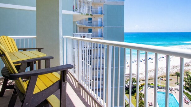A balcony with yellow chairs, a pool, and a view of the beach and ocean. - Tradewinds #1108 - Beachfront 1BR + Bunks, Gulf View, Indoor/Outdoor Pool (Orange Beach)
