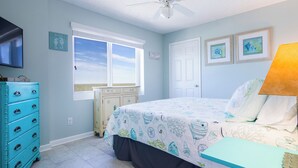 A bedroom with a bed, dresser, window, ceiling fan, and artwork on the walls. - Tradewinds #1108 - Beachfront 1BR + Bunks, Gulf View, Indoor/Outdoor Pool (Orange Beach)