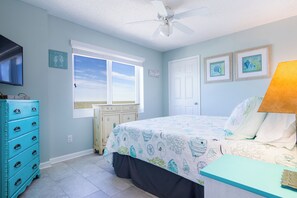A bedroom with a bed, dresser, window, ceiling fan, and artwork on the walls. - Tradewinds #1108 - Beachfront 1BR + Bunks, Gulf View, Indoor/Outdoor Pool (Orange Beach)