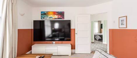 Una sala de estar con televisor, sofá, una mesa de centro y una puerta que da a otra habitación.