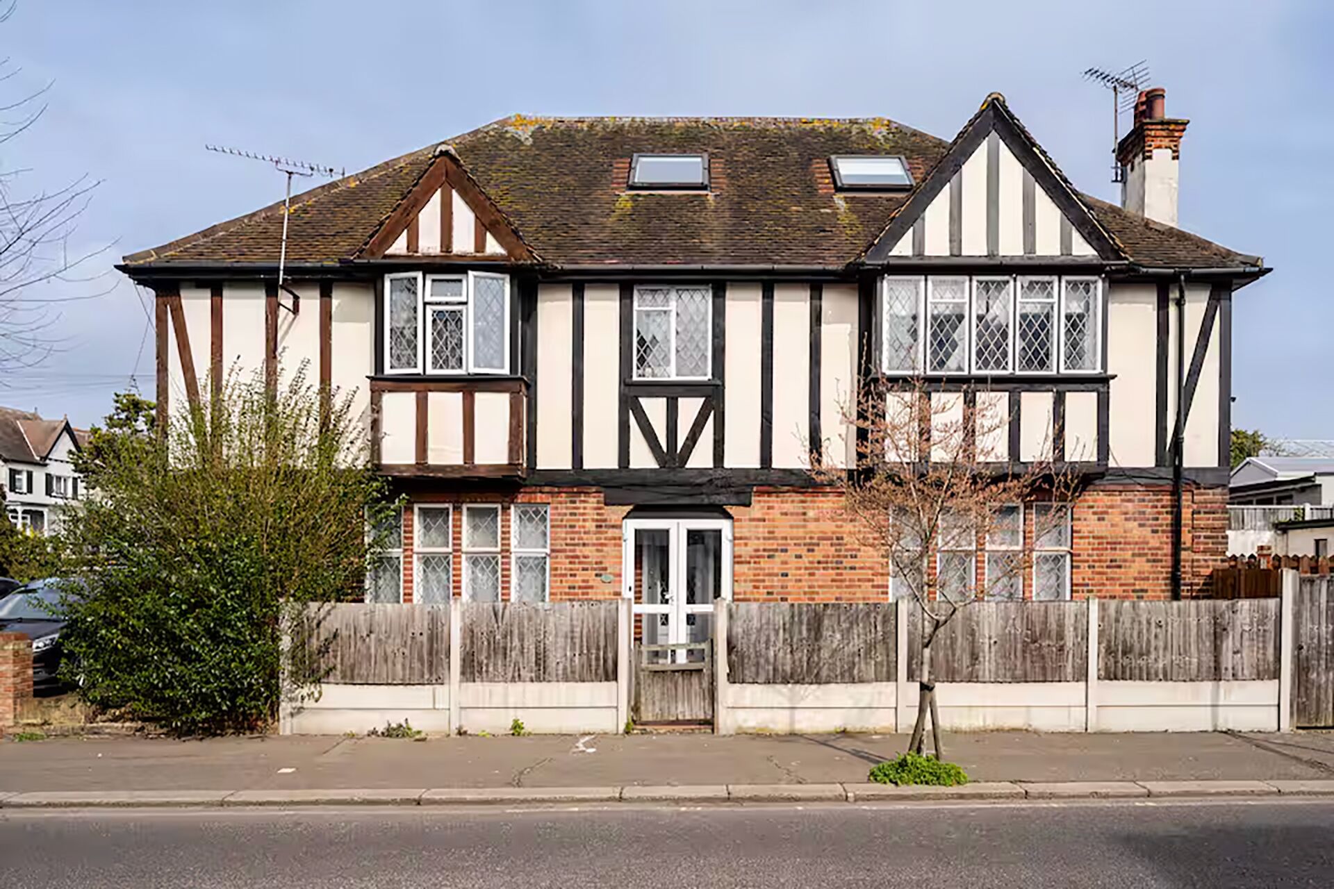 A two-story Tudor-style house with a brick facade, white-framed windows, and a wooden fence.