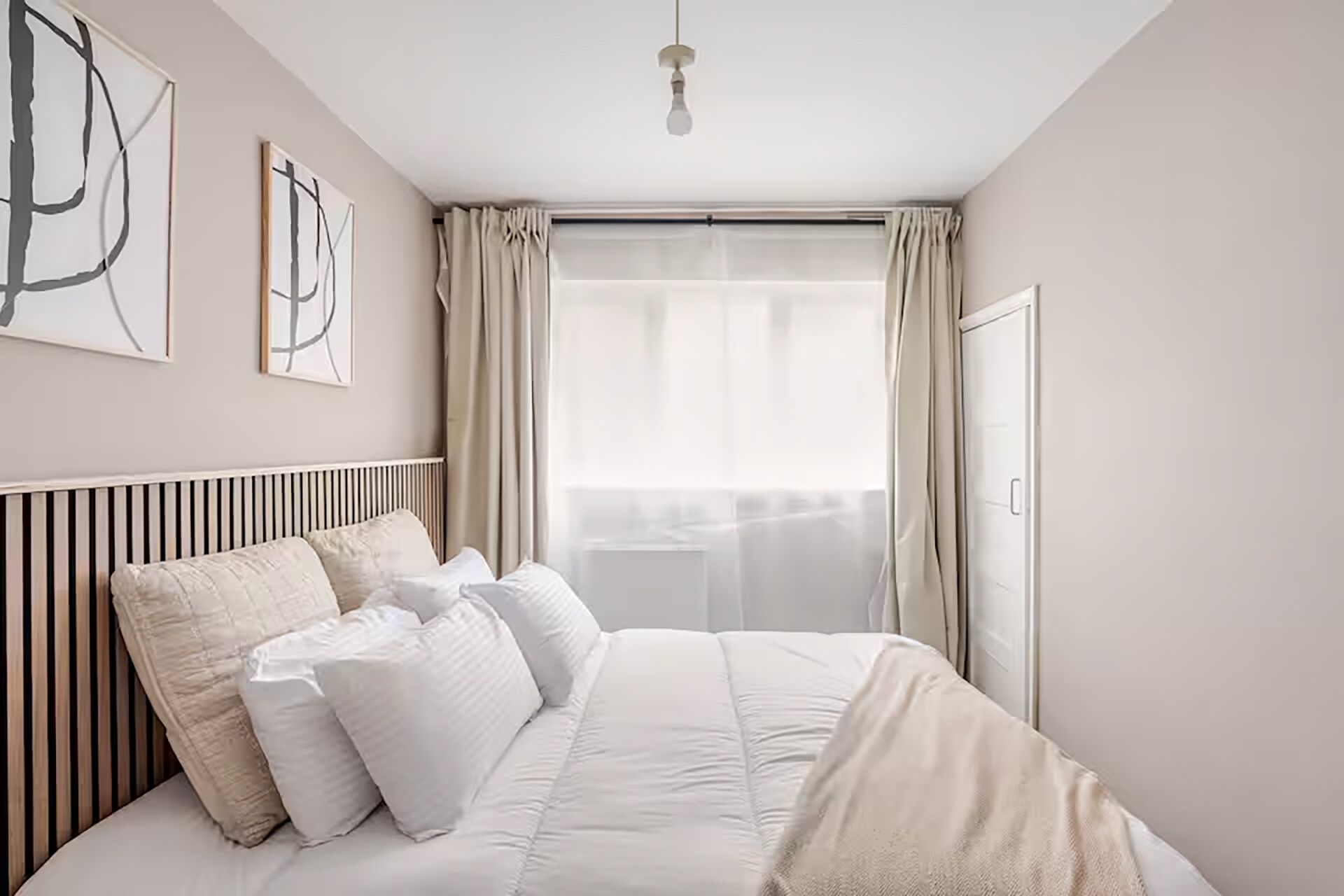 Une chambre à coucher avec un lit, des rideaux, une fenêtre et des œuvres d’art murales.