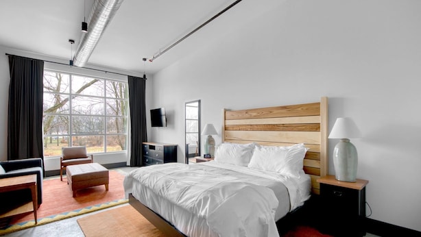 Moderni hotellihuone, jossa on suuri sänky, työpöytä, tuoli, televisio ja ikkuna, jossa on verhot.