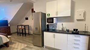 A compact kitchen with white cabinets, a microwave, and a sink. There is a small dining area with a table and chairs.