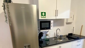 A kitchenette with a stainless steel refrigerator, a microwave, a sink, and a cabinet with a first aid sign.