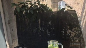 Een blauwe tafel met een karaf en twee glaasjes limonade, een zwarte stoel en een bloempot met plant.