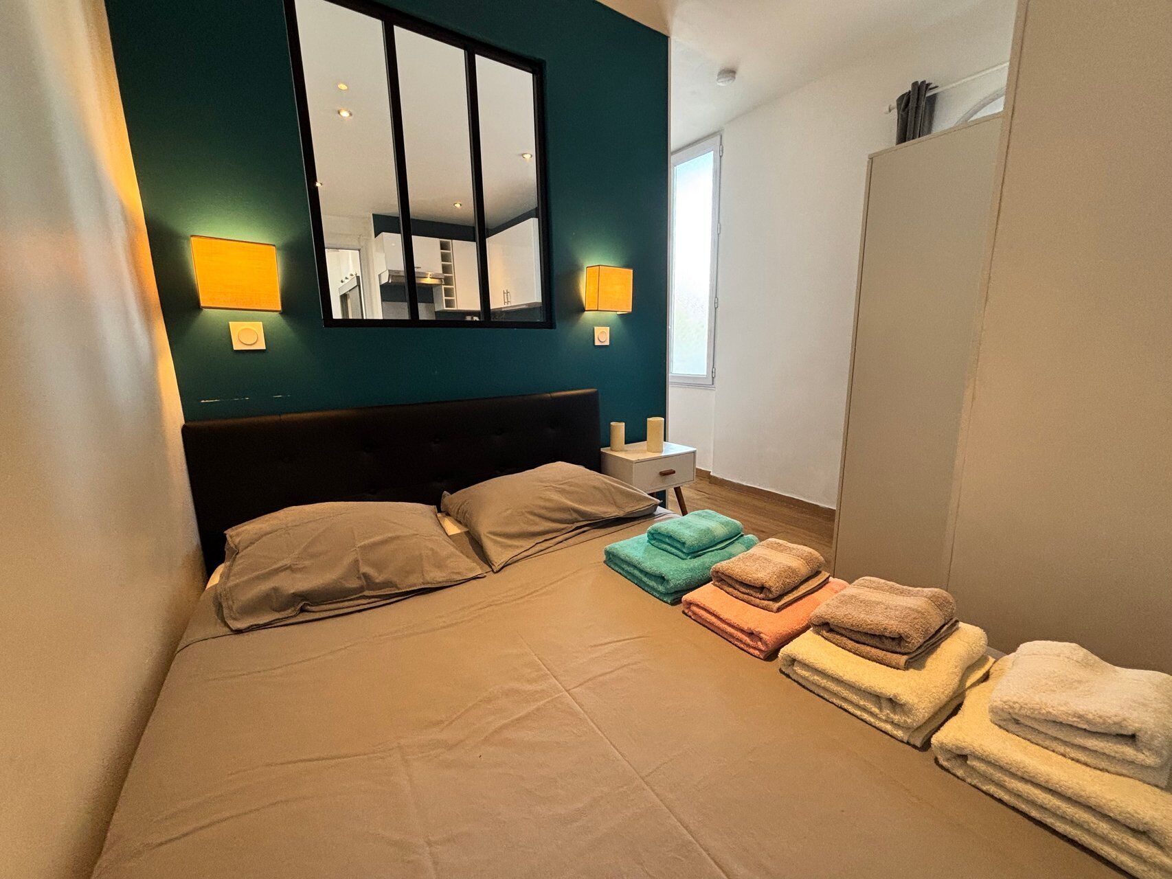 A bedroom with a bed, two bedside lamps, a mirror, and a window.