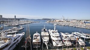 Een jachthaven met veel aangemeerde jachten, een heldere lucht en gebouwen in de verte.