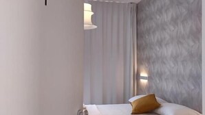 A modern hotel room with a bed, a nightstand, a wall-mounted light, and a door with a number.