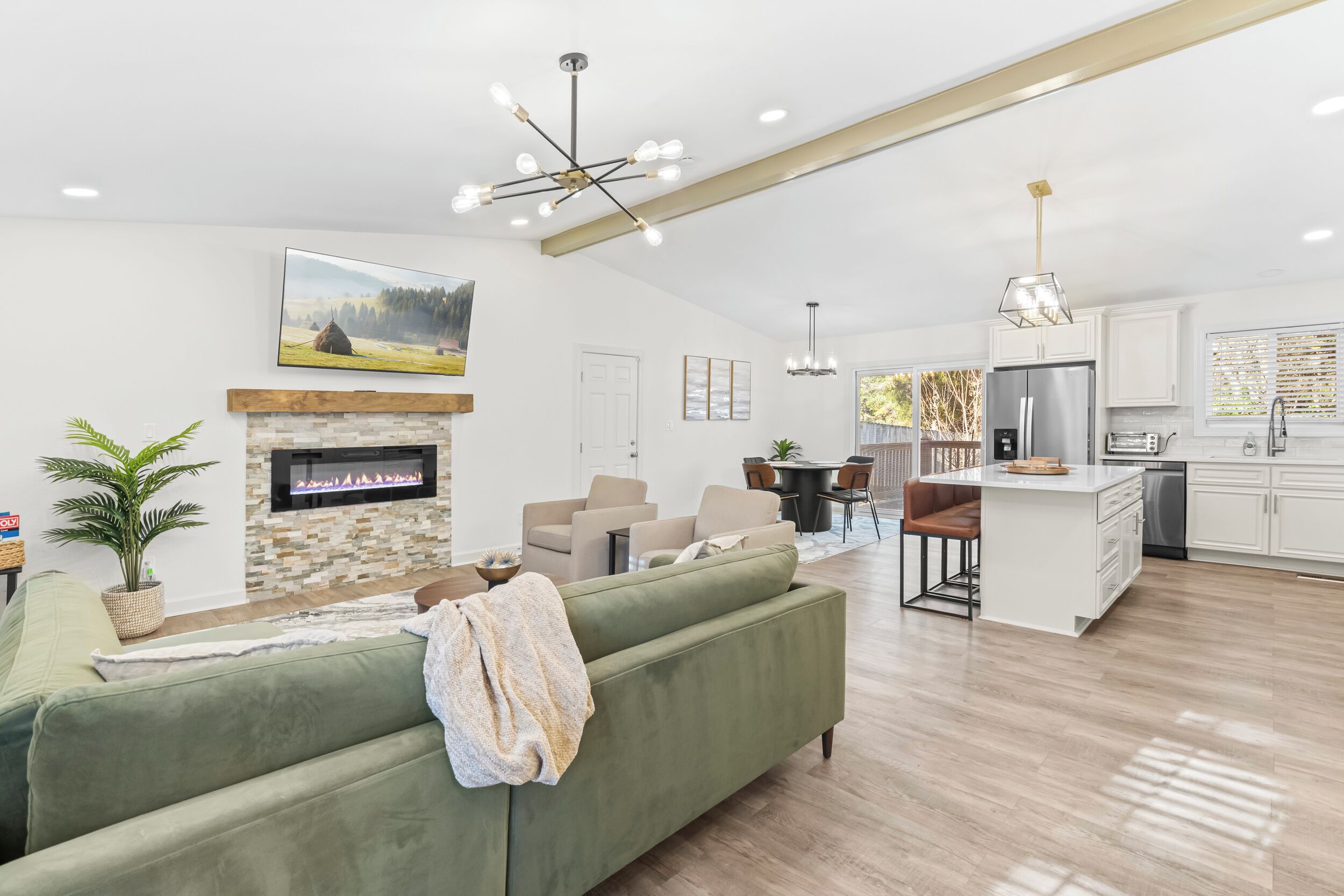 A modern living room with a fireplace, green sofa, dining area, kitchen, and a large window.