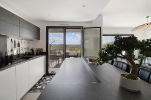 Una cocina moderna con una isla grande, un comedor con vistas y un árbol en maceta.