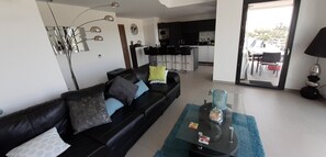 A living room with a black leather sofa, a coffee table, and a kitchen in the background. - Apartment for 4/6, 72 m² Terrace with Private Spa, Pool (Porto-Vecchio)