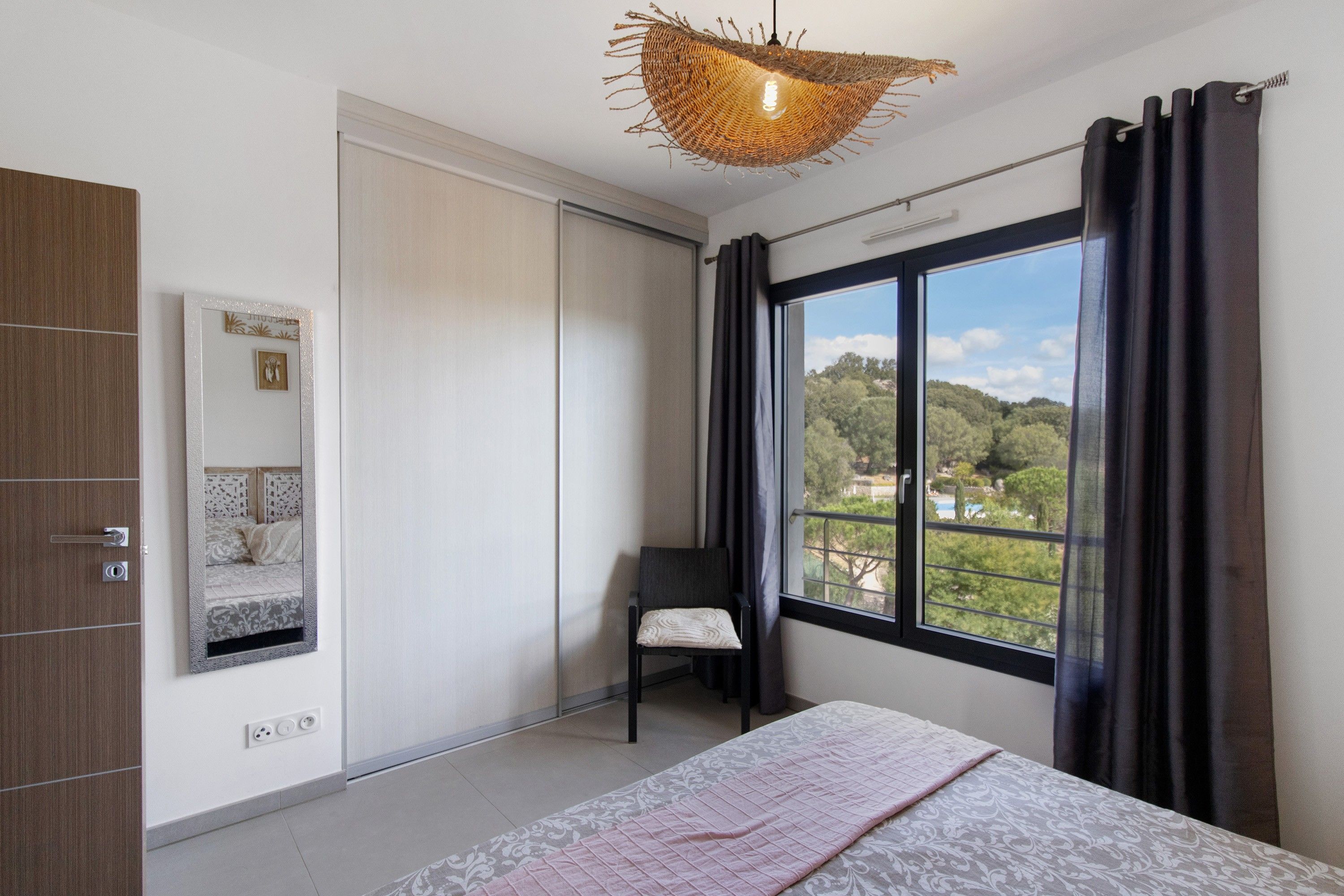 Une chambre à coucher avec un lit, une chaise, une armoire, un miroir et une fenêtre donnant sur un beau paysage.