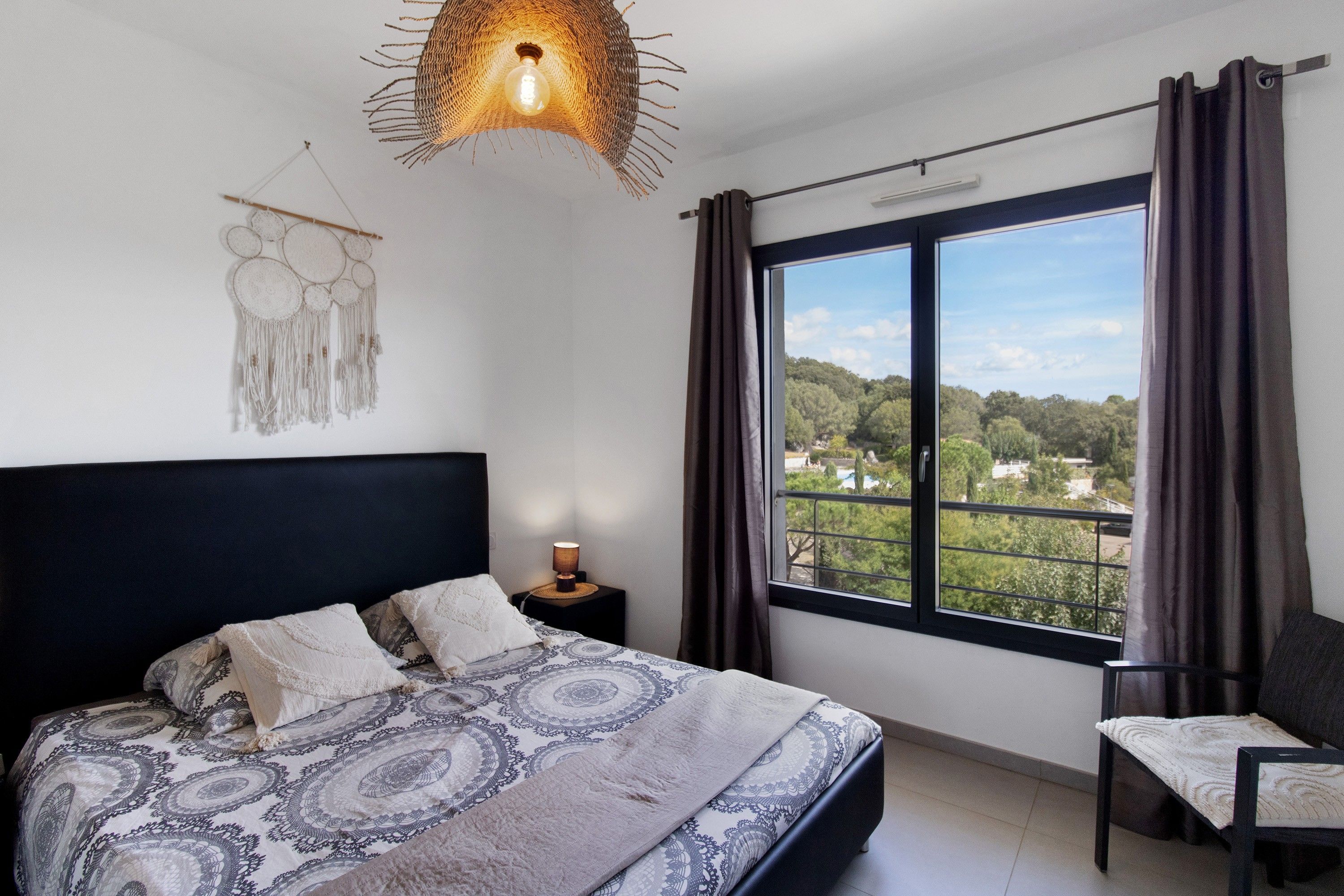 Una camera da letto con un letto grande, una lampada da comodino, vista su del verde all'esterno e un particolare lampadario.