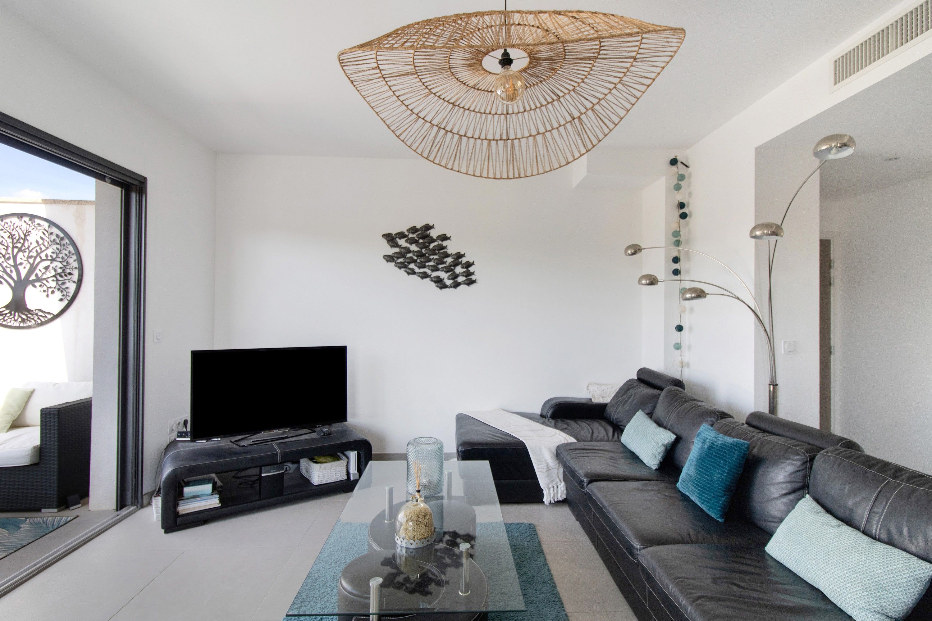 Un salon moderne doté d’un téléviseur à écran plat, d’une table basse en verre, d’un canapé en cuir et d’un luminaire original en fibres tressées.