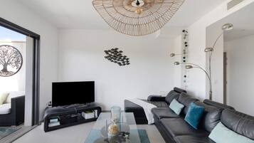 Un salon moderne doté d’un téléviseur à écran plat, d’une table basse en verre, d’un canapé en cuir et d’un luminaire original en fibres tressées.