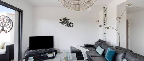 A modern living room with a flat-screen TV, a glass coffee table, a leather sofa, and a unique woven light fixture.