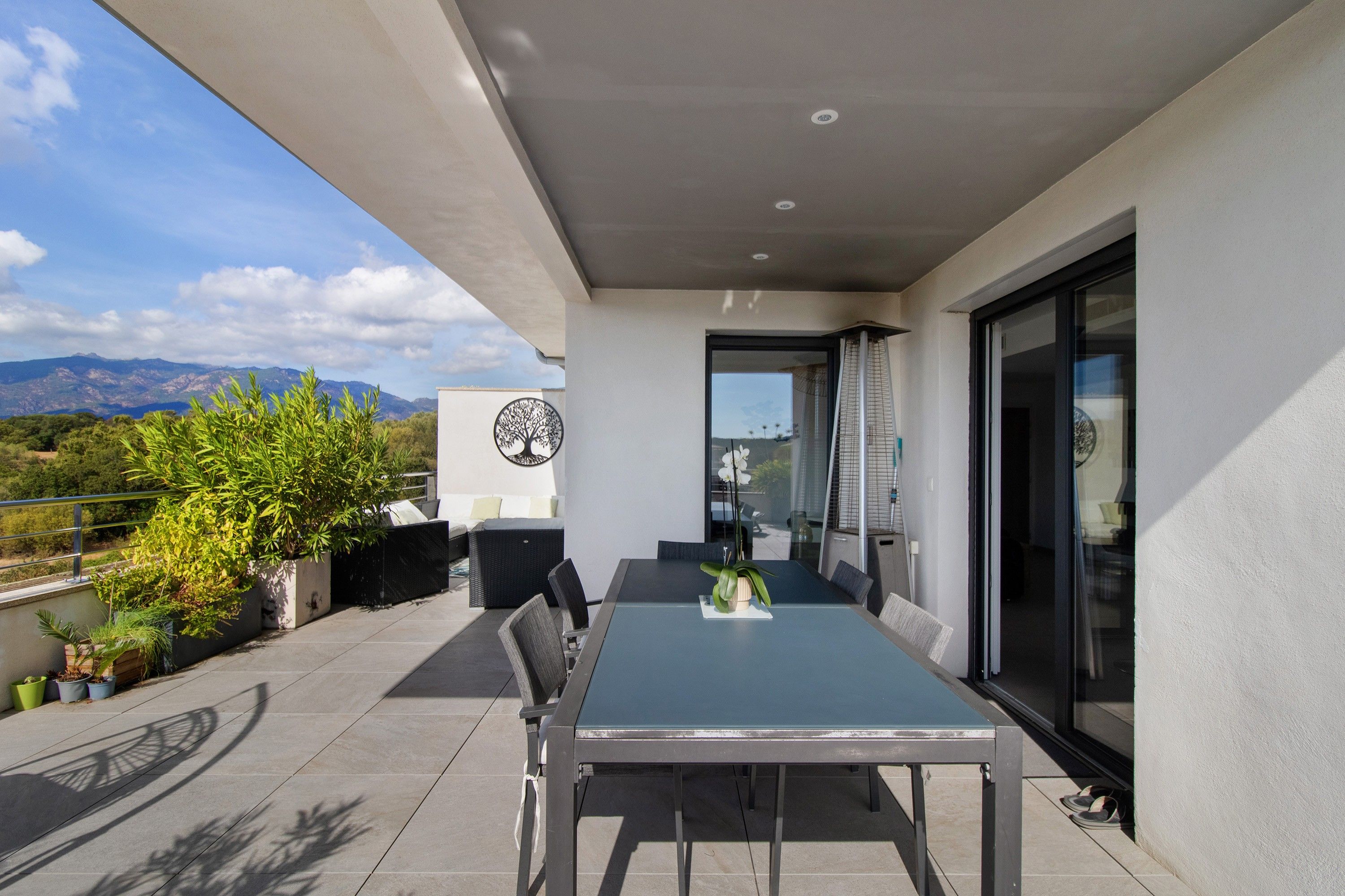 Eine moderne Außenpatio mit Esstisch und Stühlen, umgeben von Blumentöpfen und Blick auf die Berge.