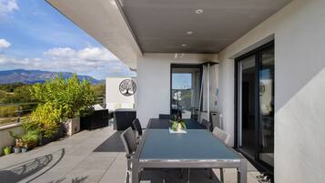 Eine moderne Außenpatio mit Esstisch und Stühlen, umgeben von Blumentöpfen und Blick auf die Berge.